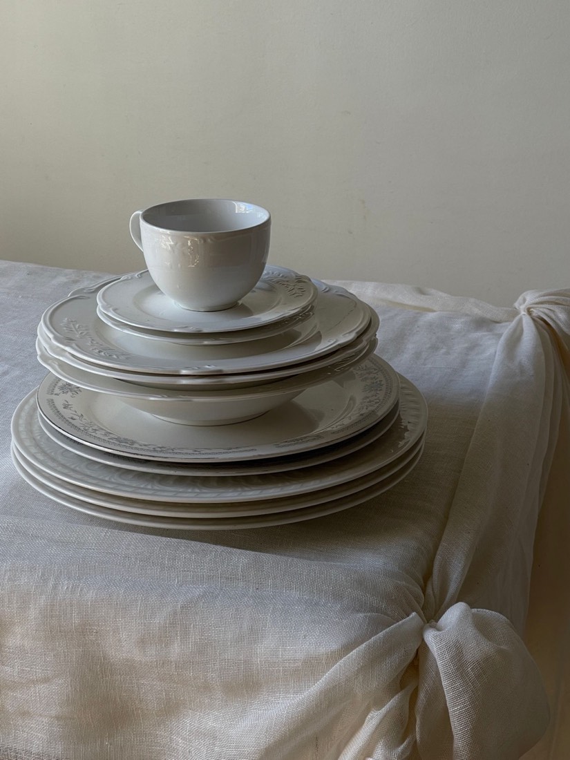 Stacked ceramic plates, bowls and a teacup on linen